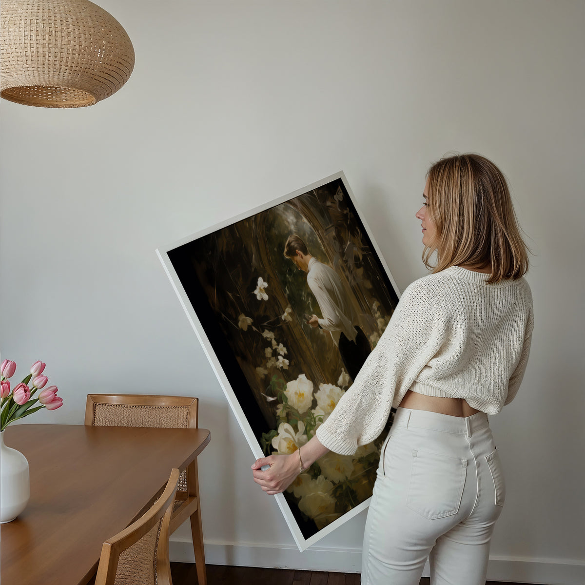 Eine Frau hält ein großes gerahmtes Poster im Essbereich mit Holzmöbeln. Motiv: Ein Mann im weißen Hemd neben weißen Rosen vor einem dunklen Spiegel.