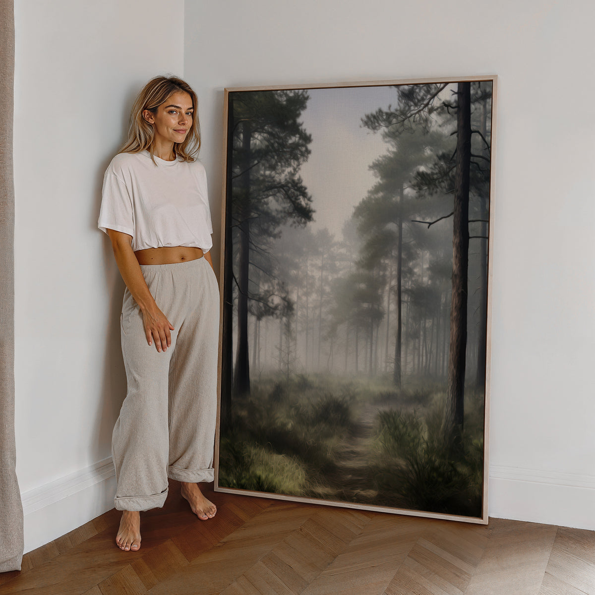 Eine Frau steht neben einem großen gerahmten Poster. Motiv: Hohe Kiefern an einem stillen Waldweg im Nebel.