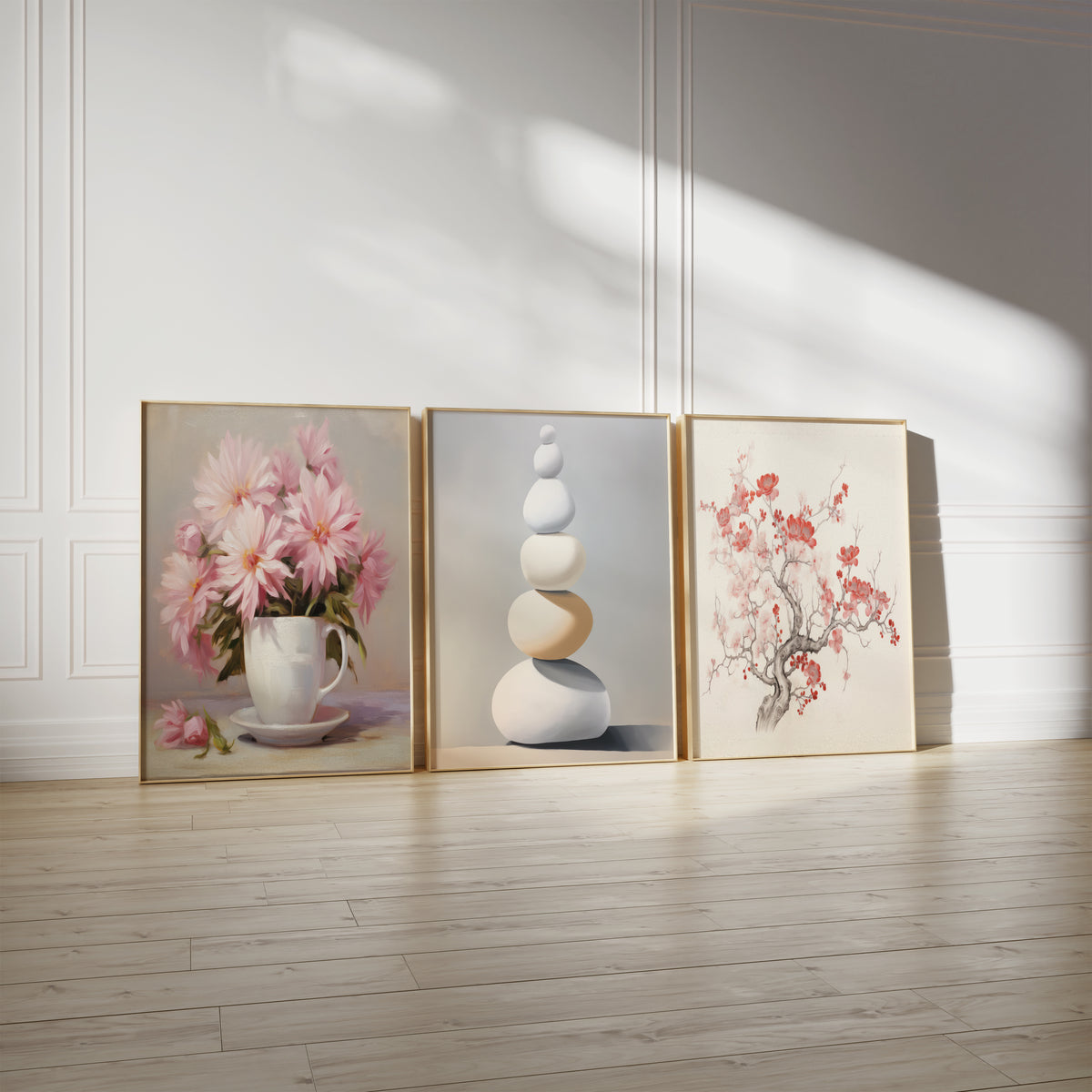 Drei gerahmte Poster an einer hellen Wand mit Zierleisten. Motive: Rosa Blüten in einer weißen Tasse auf einer Untertasse; Sanft gerundete Steine in Weiß, Beige und Grau zu einem Turm gestapelt; Geschwungener Zweig mit roten und rosa Kirschblüten auf hellem Grund.