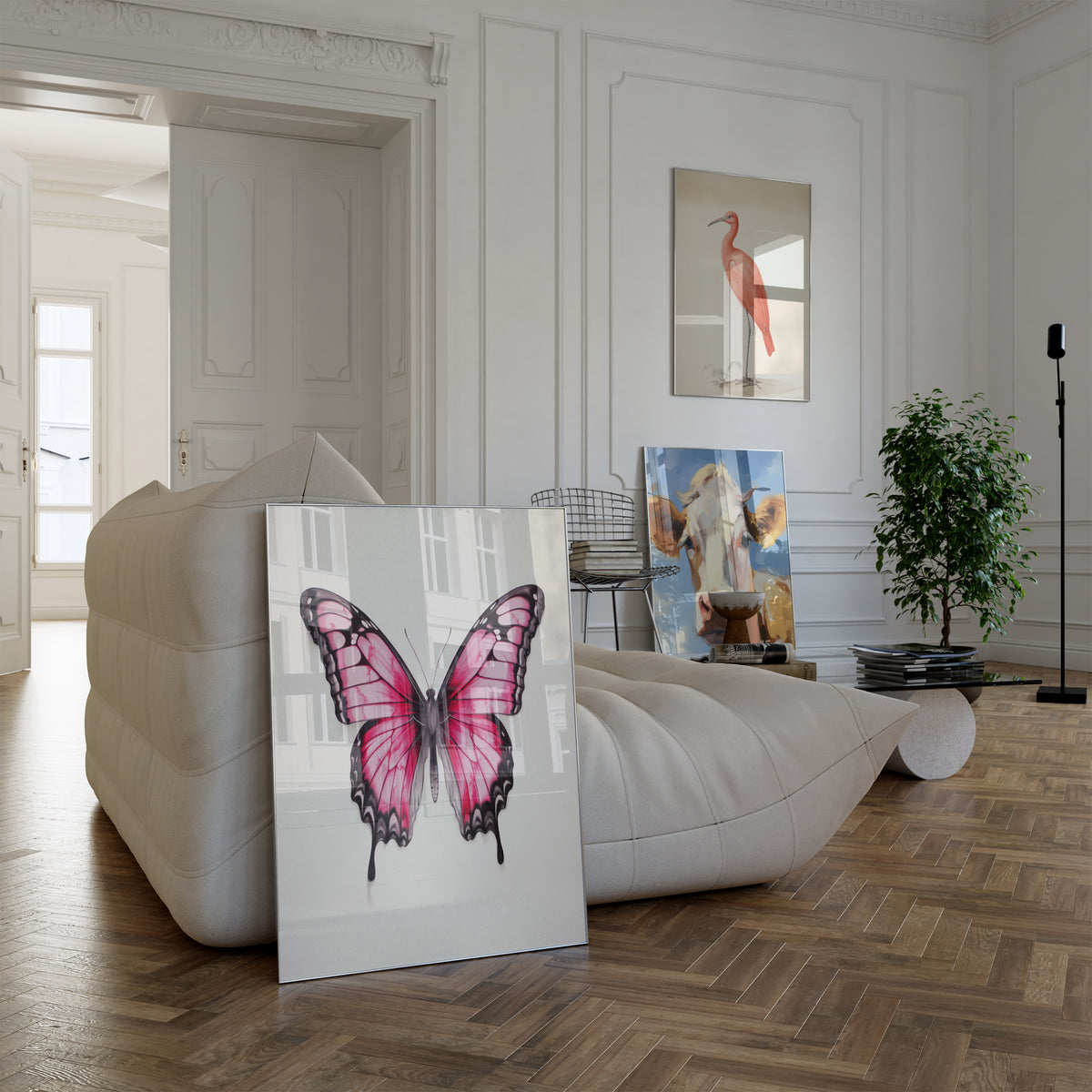 Poster in einem hellen Wohnzimmer mit weißem Sofa. Motive: Rosa Schmetterling mit schwarz umrandeten Flügeln auf hellem Hintergrund; Roter Ibis mit langem gebogenem Schnabel vor cremefarbenem Hintergrund; Porträt einer braun-weißen Kuh unter blauem Himmel.