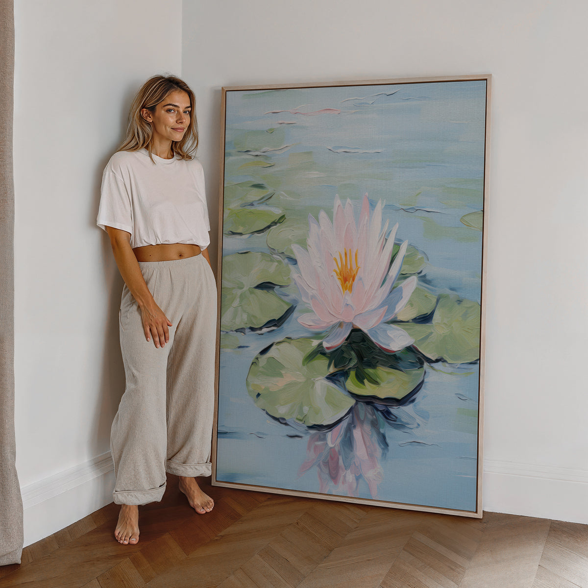 Eine Frau steht neben einem großen gerahmten Poster. Motiv: Rosa Seerose mit grünen Blättern auf hellblauem Wasser.