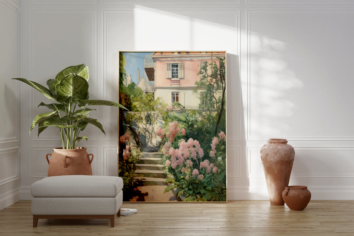 Großes gerahmtes Poster an einer hellen Wohnzimmerwand neben Sessel, Pflanze und Vase. Motiv: Steintreppe mit rosa Blüten vor einem hellen Haus.