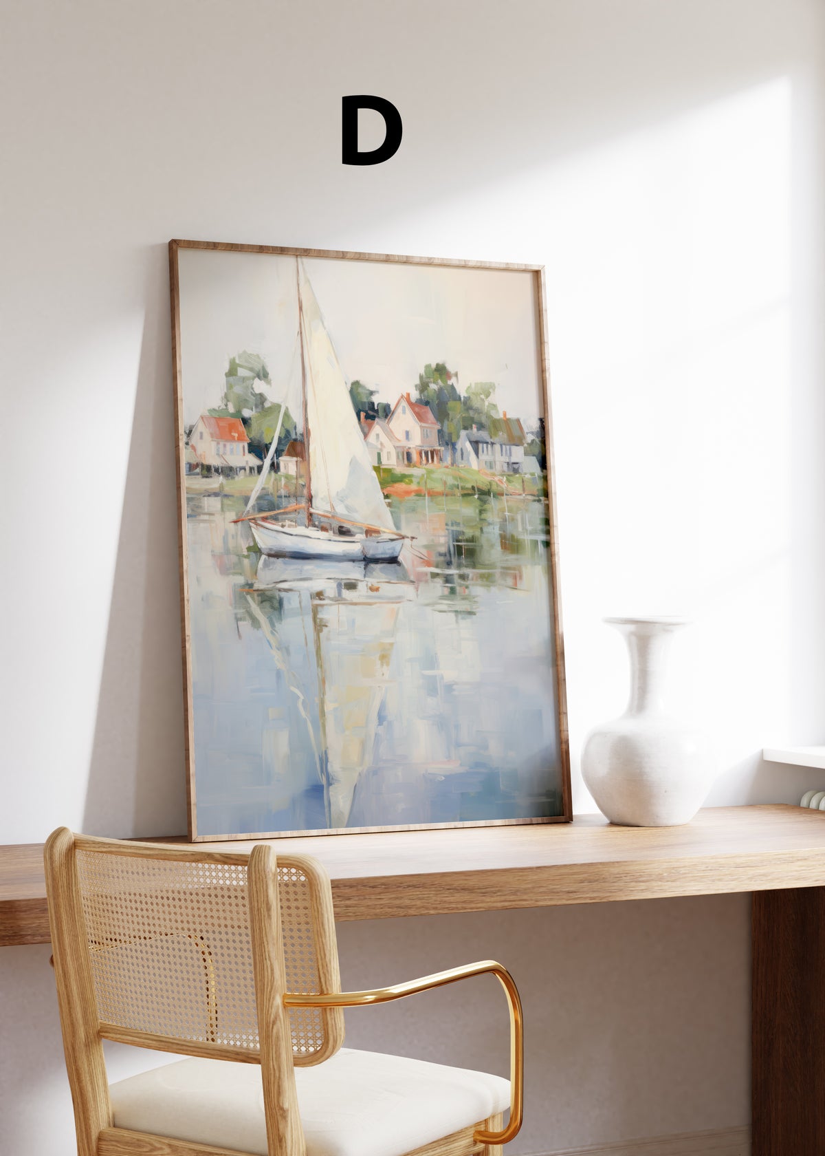Postermotiv D: Segelboot mit weißem Segel vor kleinen Häusern am Wasser. Im Holzrahmen auf einem Schreibtisch.