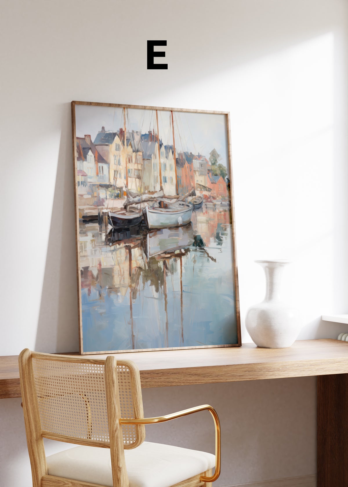 Postermotiv E: Segelboote vor pastellfarbenen Hafenhäusern mit Spiegelungen im Wasser. Im Holzrahmen auf einem Schreibtisch.