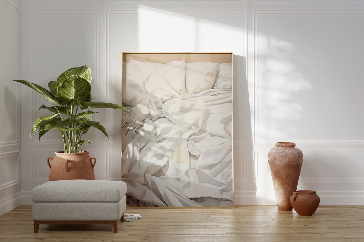 Großes gerahmtes Poster an einer hellen Wohnzimmerwand neben Sessel, Pflanze und Vase. Motiv: Malerische Darstellung weißer Kissen und gefalteter Bettwäsche.