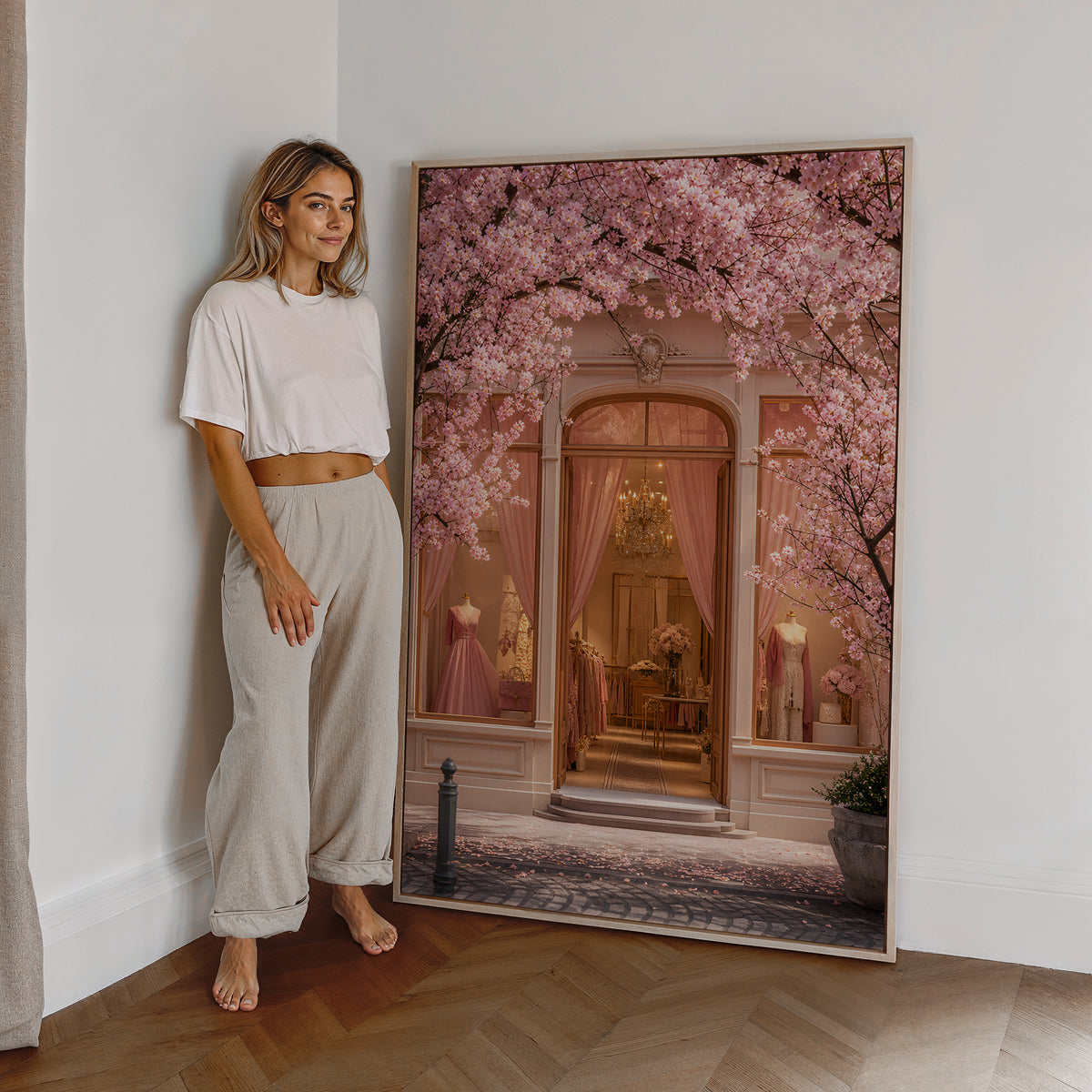 Motiv mit einer rosafarbenen Boutique unter blühenden Kirschzweigen, als großes gerahmtes Wandbild neben einer Frau.