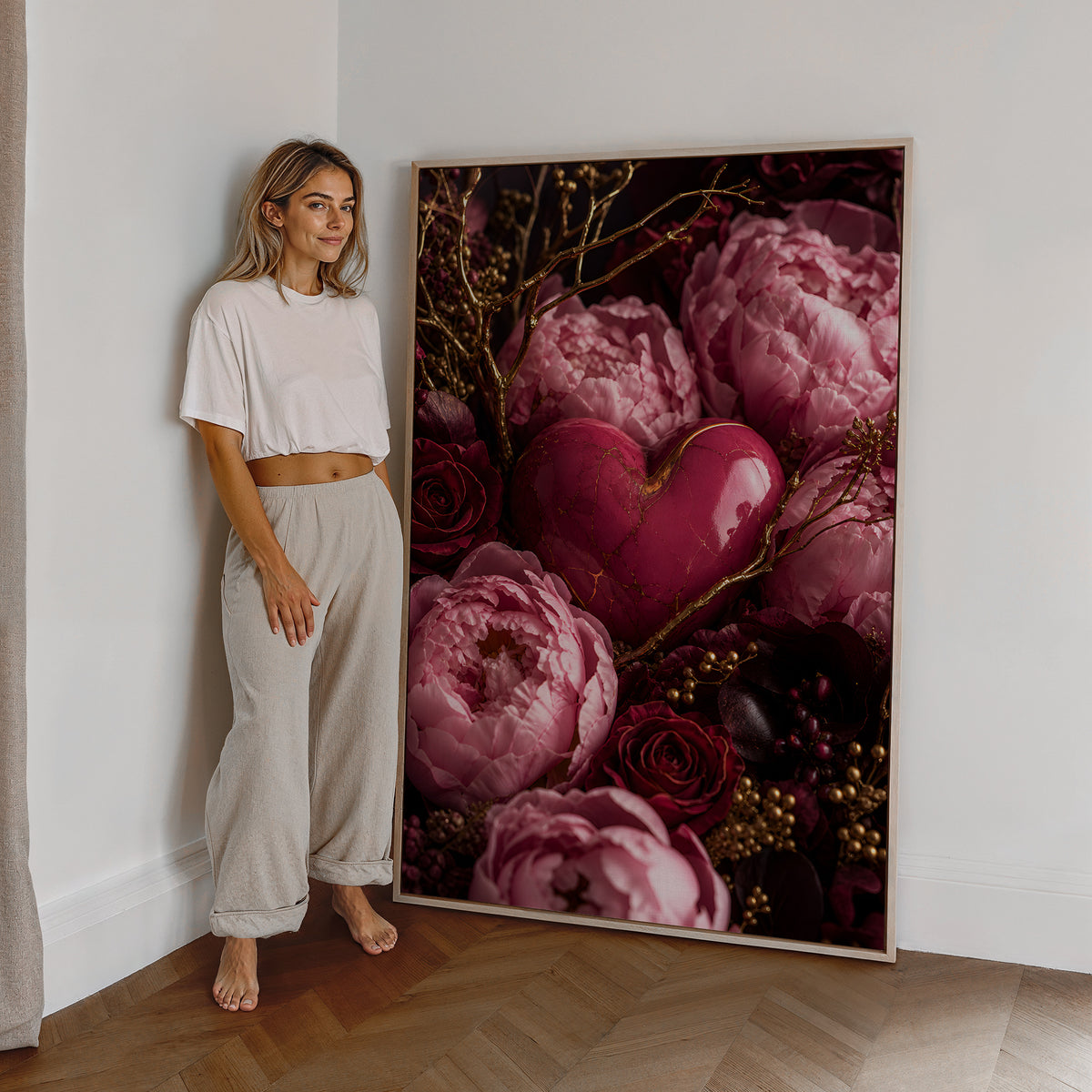 Motiv mit einem rosafarbenen Herz zwischen pinken Pfingstrosen, dunklen Rosen und goldenen Zweigen, als großes gerahmtes Wandbild neben einer Frau.