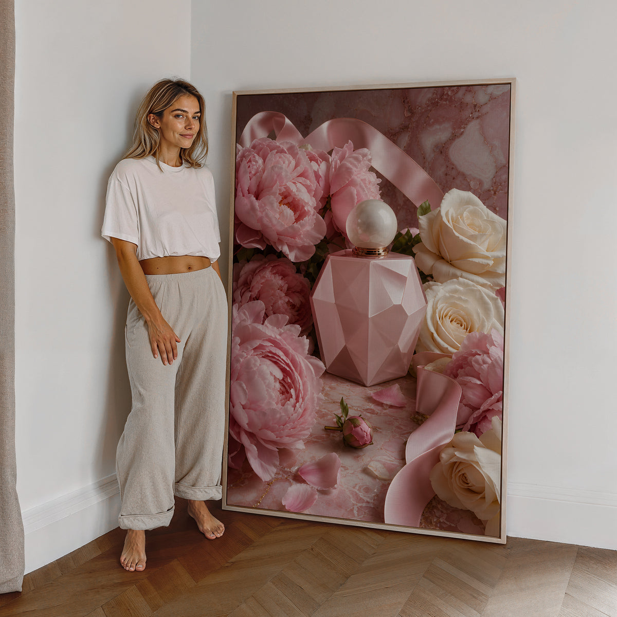 Motiv mit rosafarbenem Parfumflakon zwischen Pfingstrosen, weißen Rosen und Satinbändern, als großes gerahmtes Wandbild neben einer Frau.