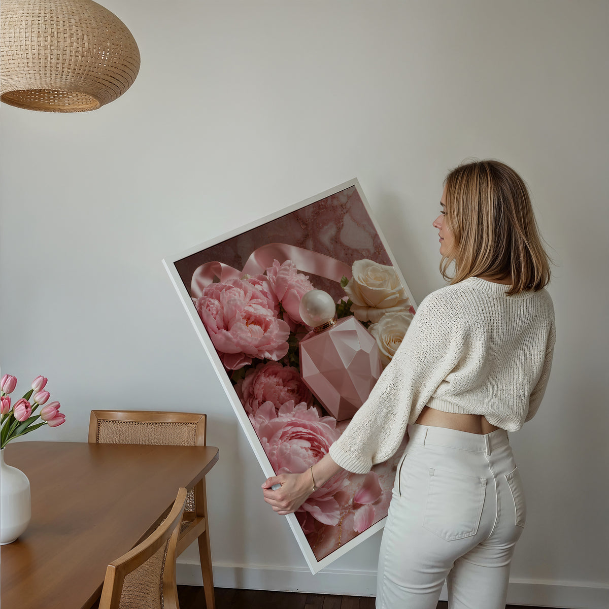 Motiv mit rosafarbenem Parfumflakon zwischen Pfingstrosen, weißen Rosen und Satinbändern, als gerahmtes Poster in den Händen einer Frau.