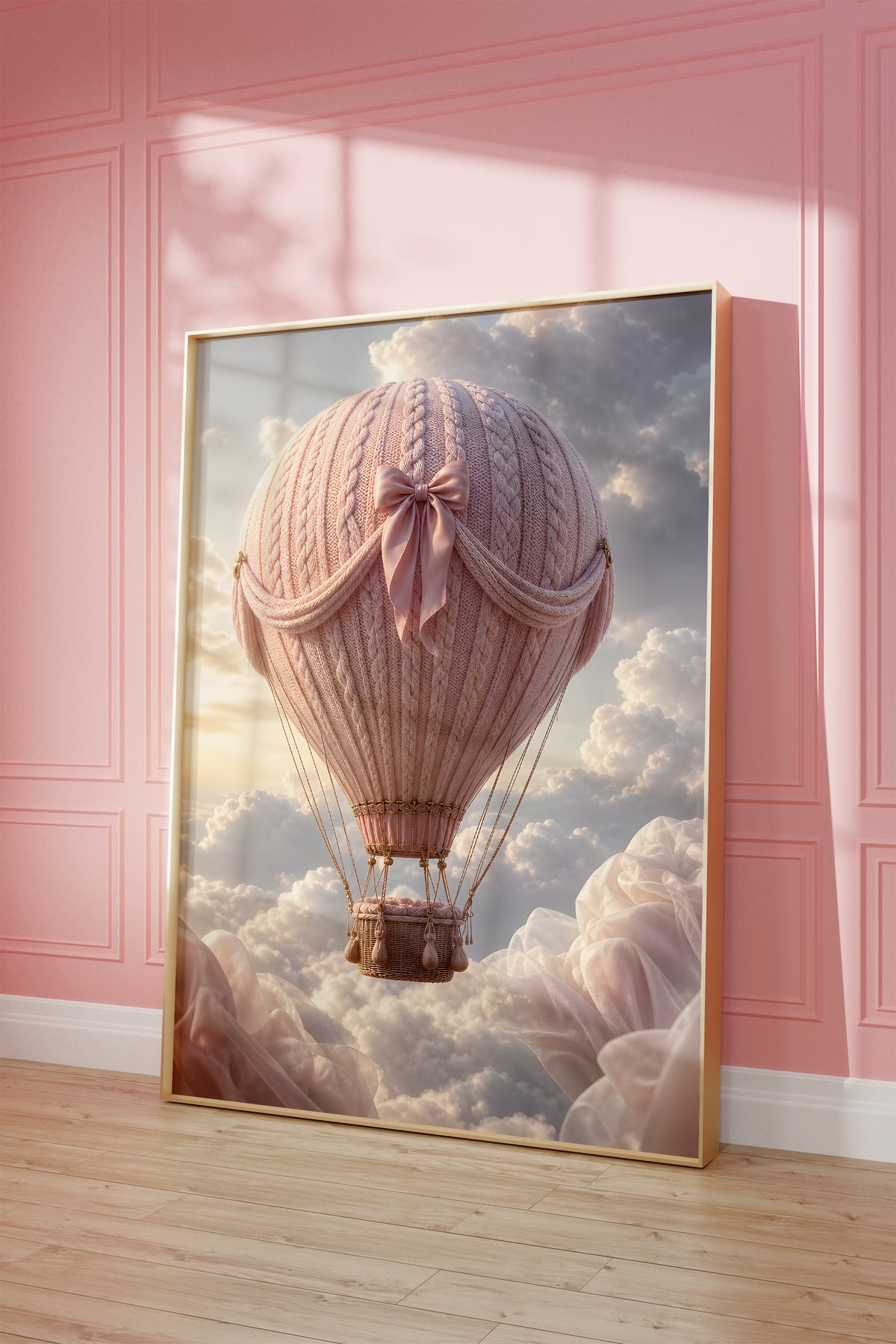 Motiv mit einem rosafarbenen Heißluftballon in Strickoptik mit Satinschleife über Wolken, als gerahmtes Poster vor einer rosafarbenen Wand.