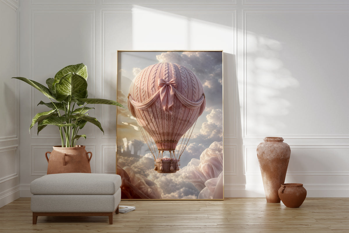 Motiv mit einem rosafarbenen Heißluftballon in Strickoptik mit Satinschleife über Wolken, als gerahmtes Poster neben Sessel und Zimmerpflanze.
