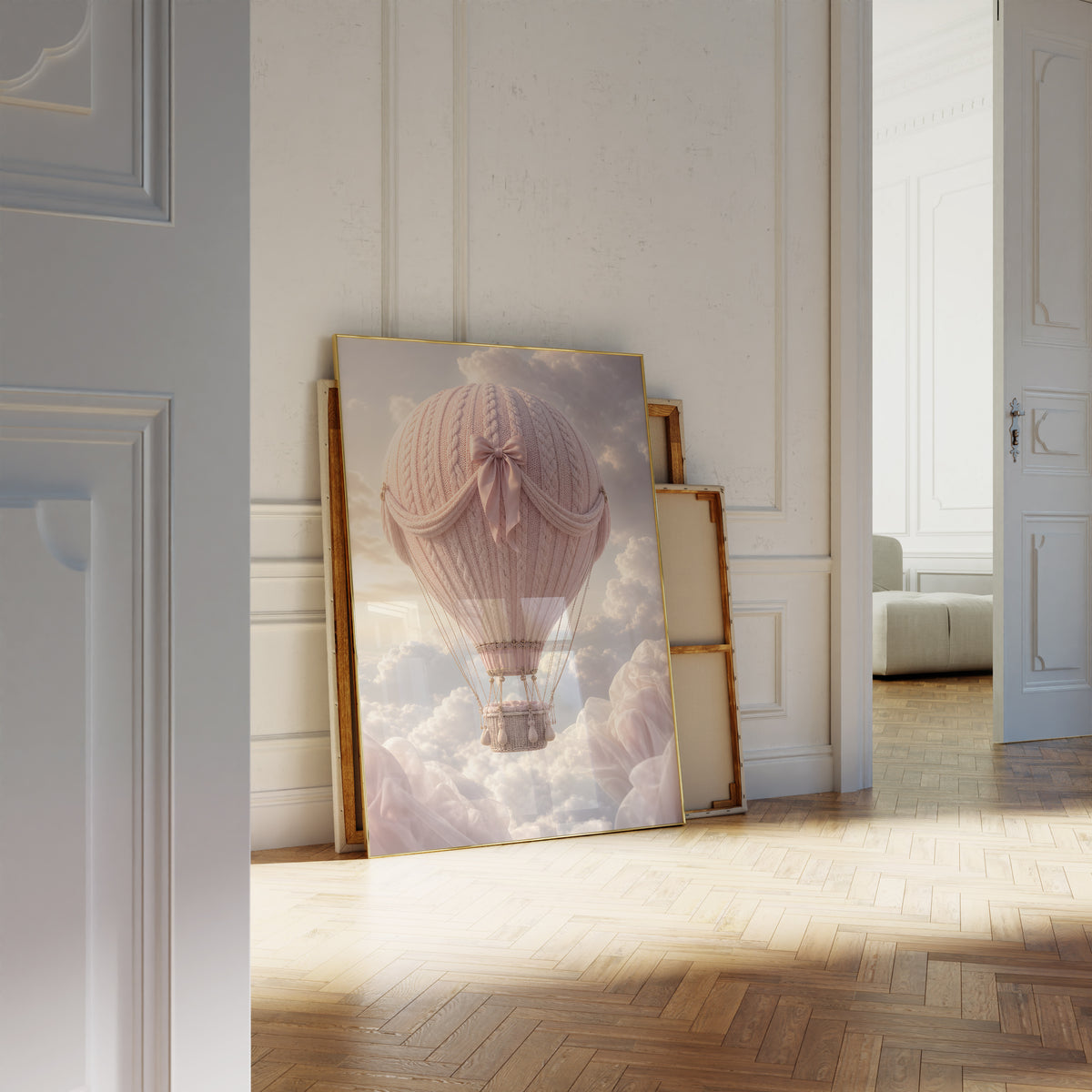 Motiv mit einem rosafarbenen Heißluftballon in Strickoptik mit Satinschleife über Wolken, als an die Wand gelehntes Poster neben leeren Rahmen.