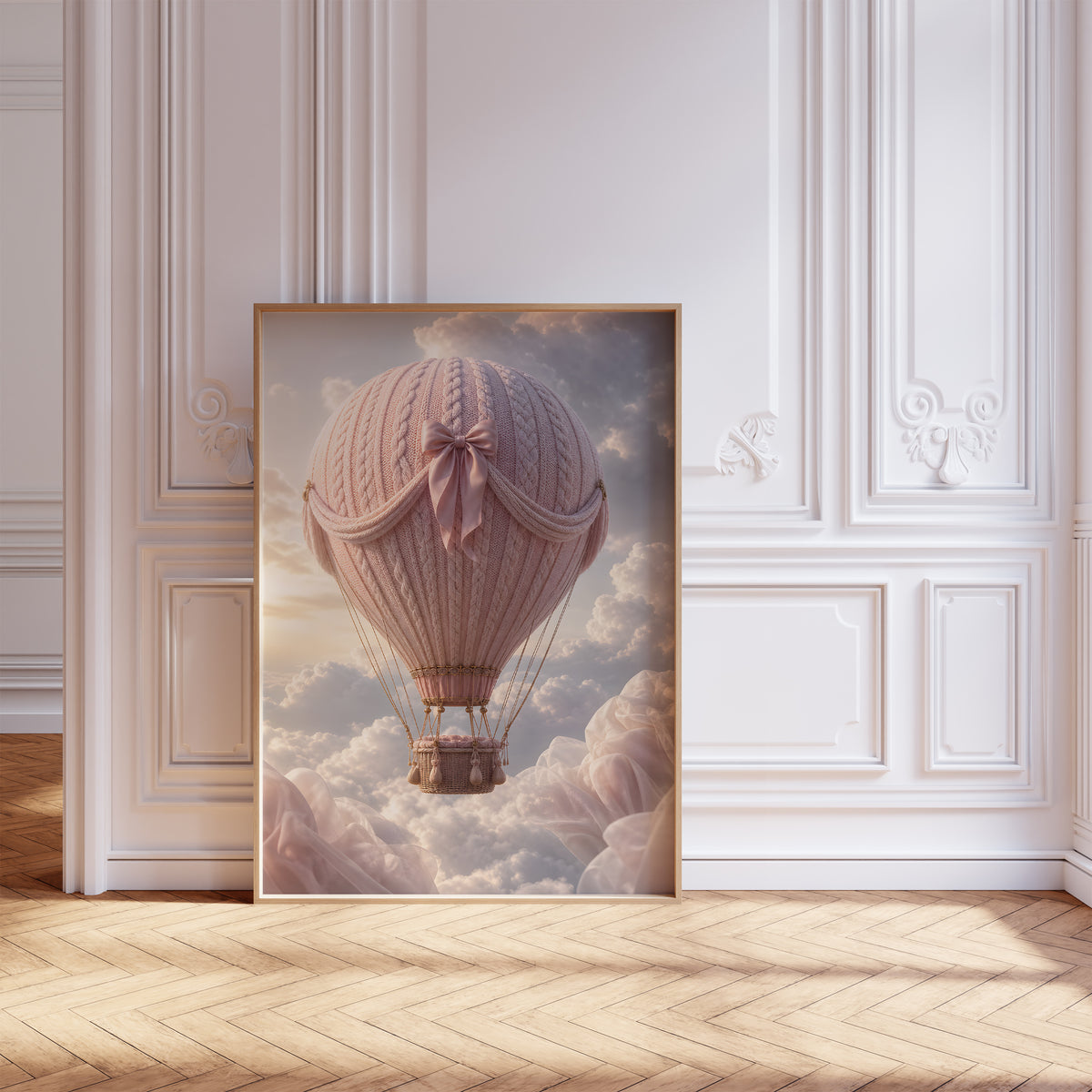 Gerahmtes Poster mit einem rosafarbenen Heißluftballon in Strickoptik mit Satinschleife über Wolken, vor einer weißen Wand mit Zierleisten.