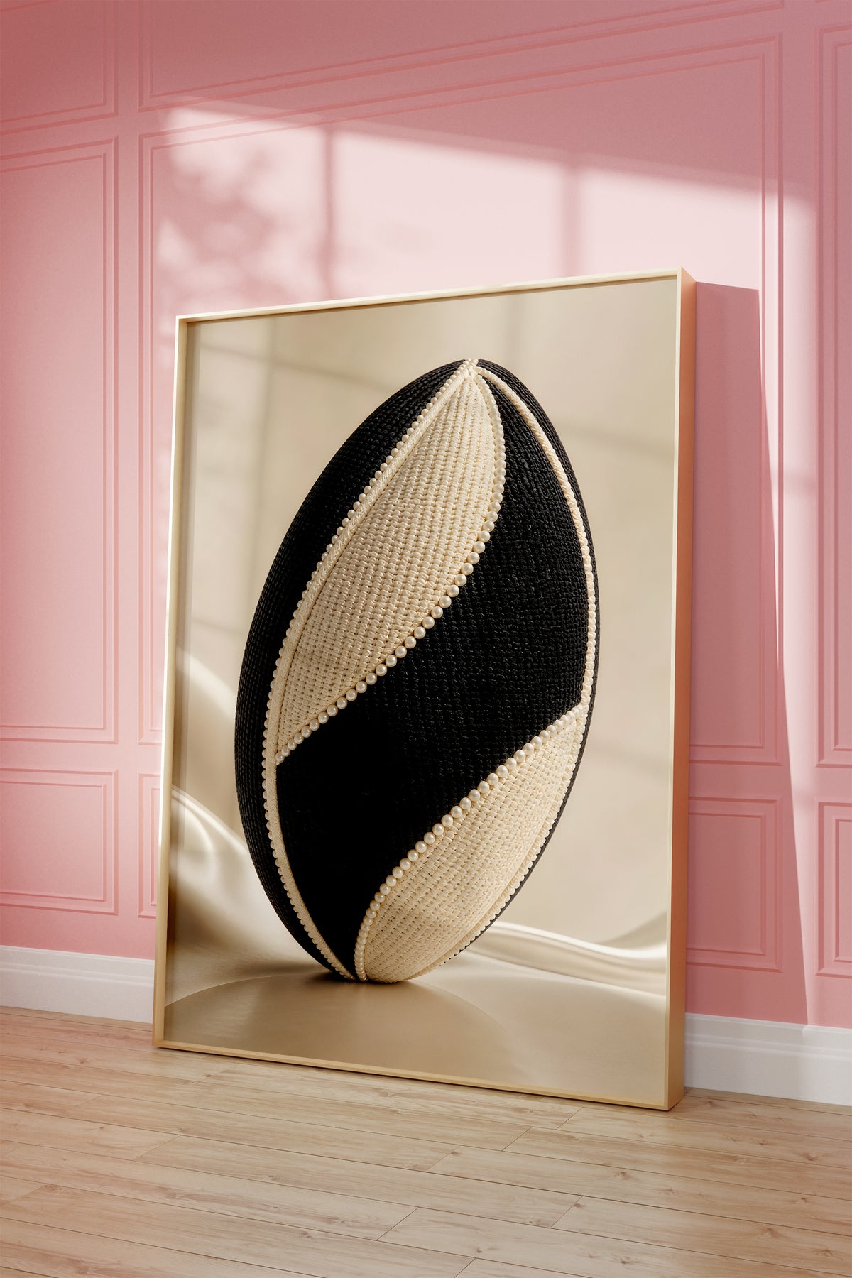 Motiv mit einem schwarz-weißen Rugbyball in Tweedoptik mit Perlenbesatz, als gerahmtes Poster vor einer rosafarbenen Wand.