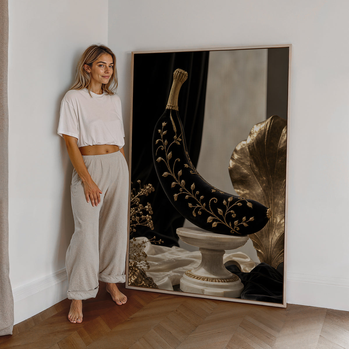 Motiv mit einer schwarzen Banane mit goldenen Ranken auf einem Marmorsockel, als großes gerahmtes Wandbild neben einer Frau.