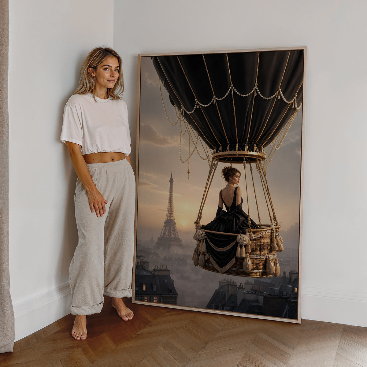 Motiv mit einer Frau im schwarzen Kleid im Korb eines schwarzen Heißluftballons über Paris, als großes gerahmtes Wandbild neben einer Frau.
