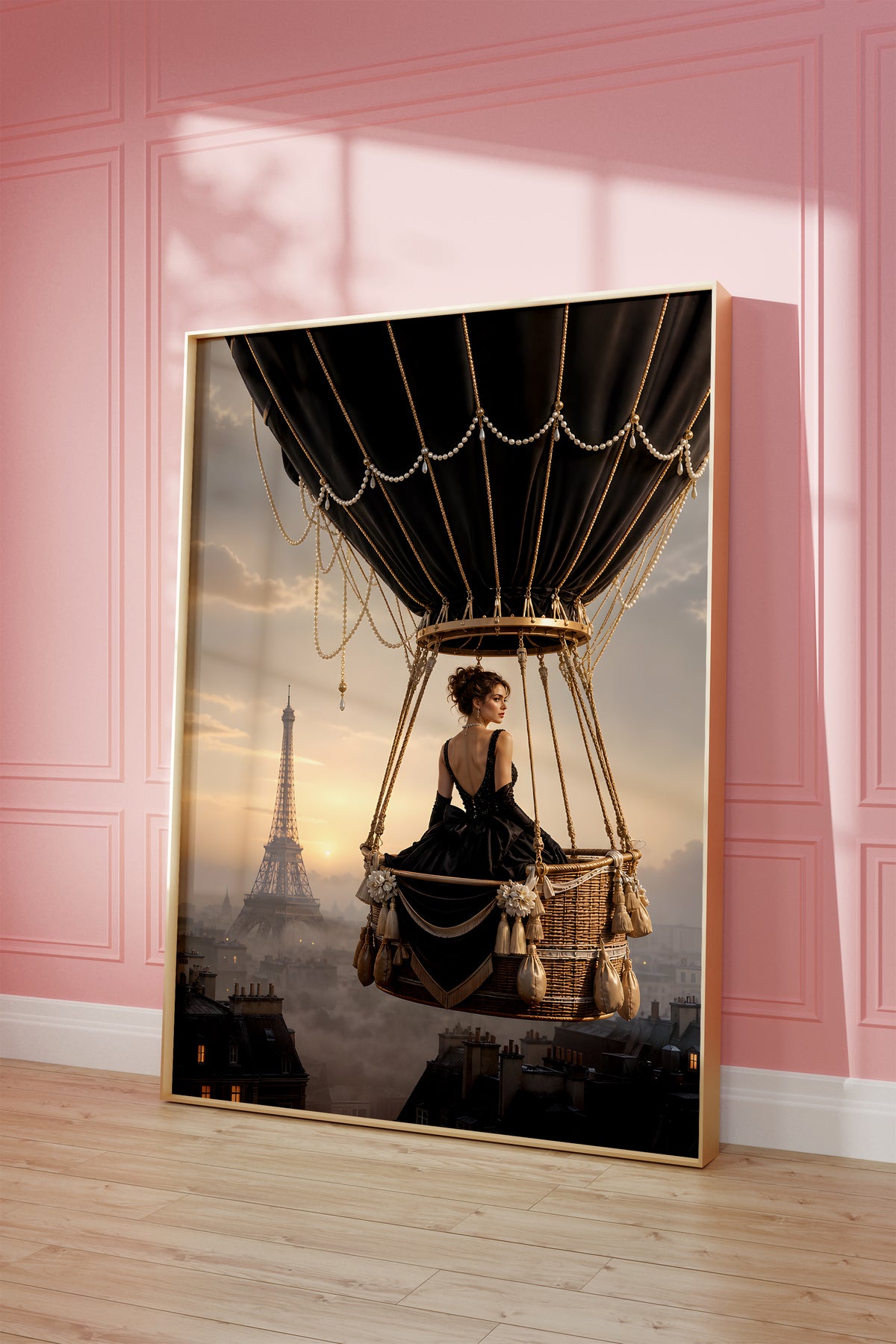 Motiv mit einer Frau im schwarzen Kleid im Korb eines schwarzen Heißluftballons über Paris, als gerahmtes Poster vor einer rosafarbenen Wand.