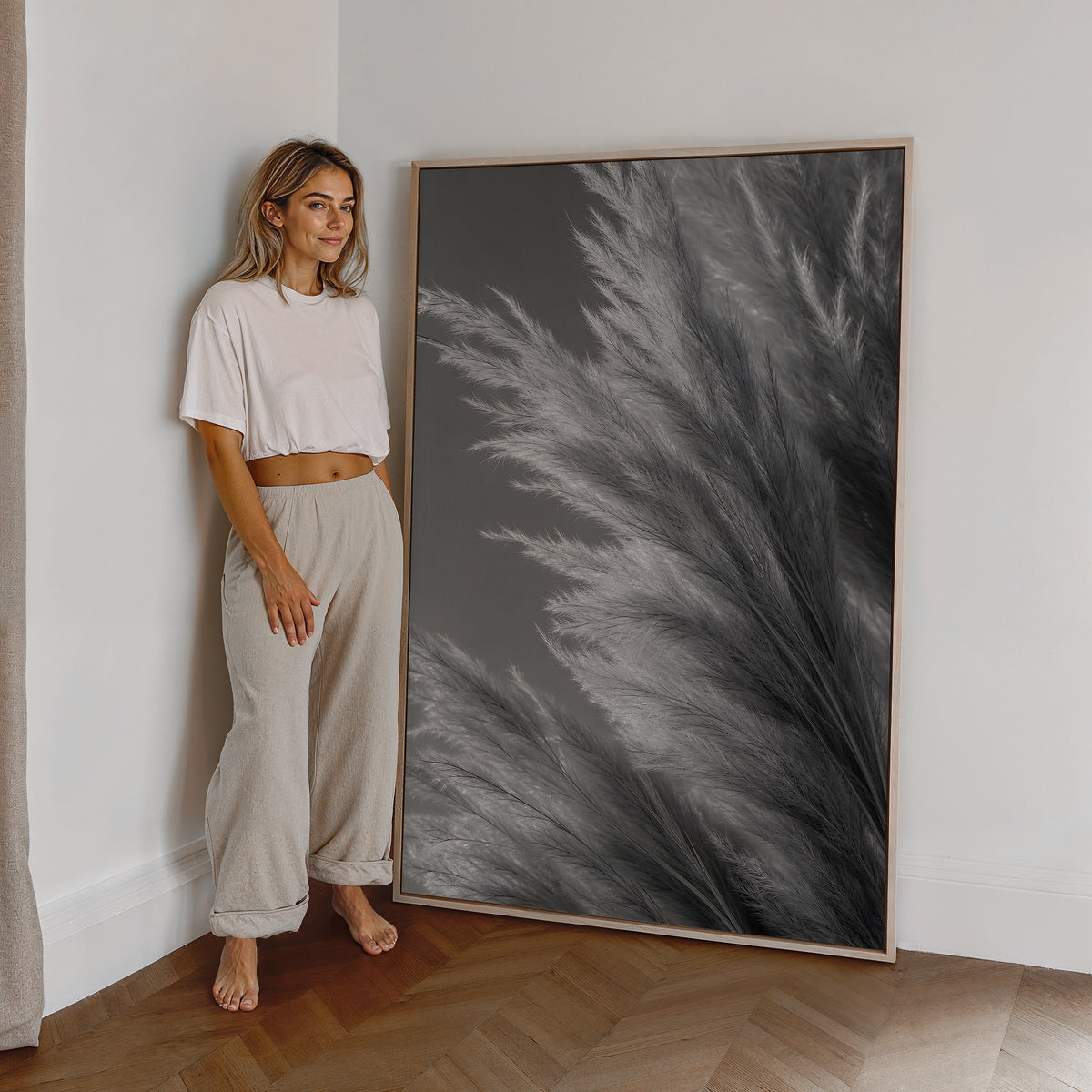 Motiv mit silbergrauen Pampasfasern in einer dichten monochromen Nahaufnahme, als großes gerahmtes Wandbild neben einer Frau.
