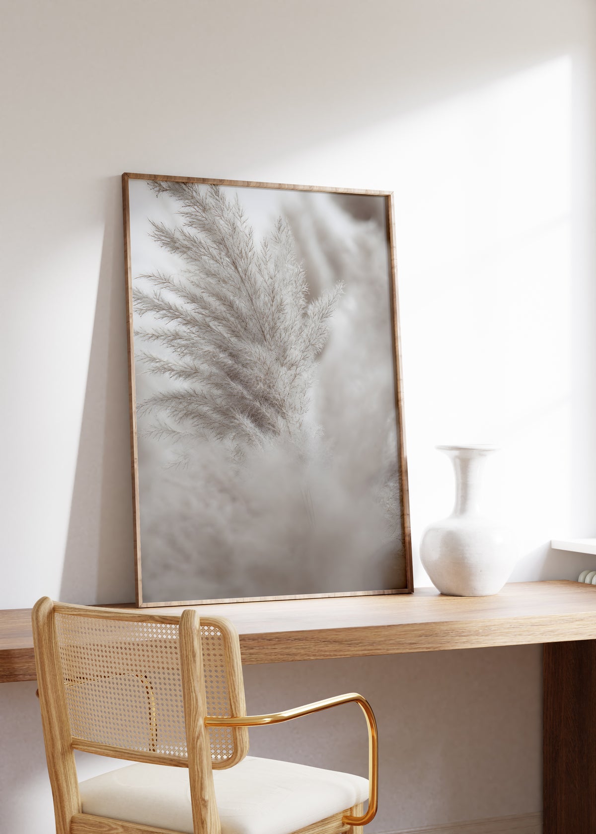 Gerahmtes Poster mit einem silbergrauen Pampaswedel vor weich verschwommenem Hintergrund, auf einem Holztisch neben einer weißen Vase.