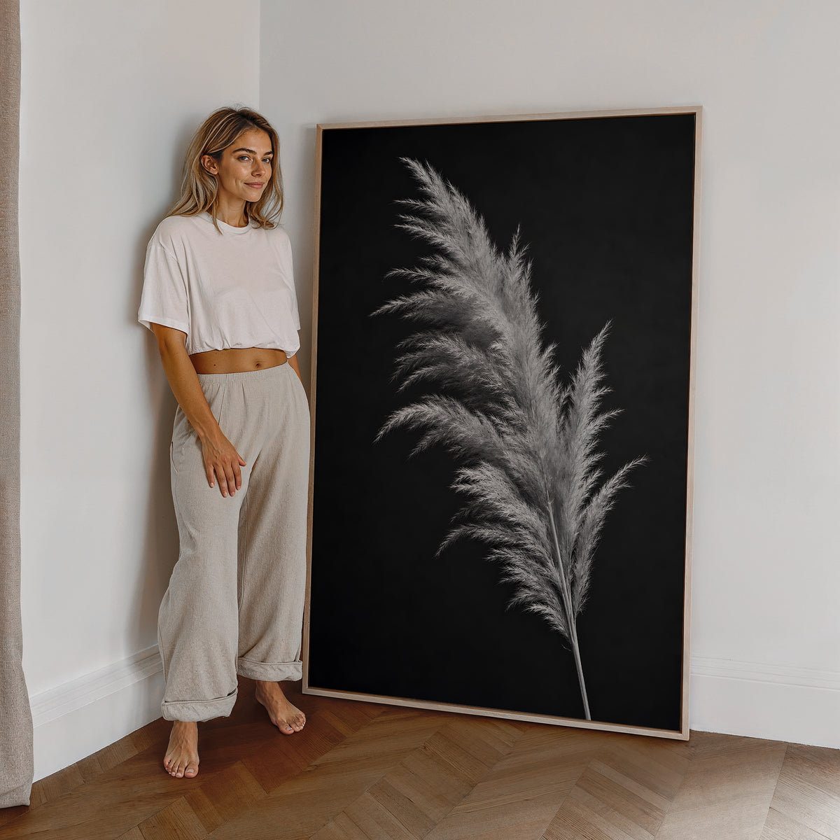 Motiv mit einem silbrig hellen Pampaswedel vor schwarzem Hintergrund, als großes gerahmtes Wandbild neben einer Frau.