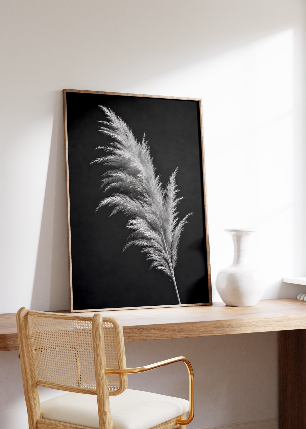 Gerahmtes Poster mit einem silbrig hellen Pampaswedel vor schwarzem Hintergrund, auf einem Holztisch neben einer weißen Vase.