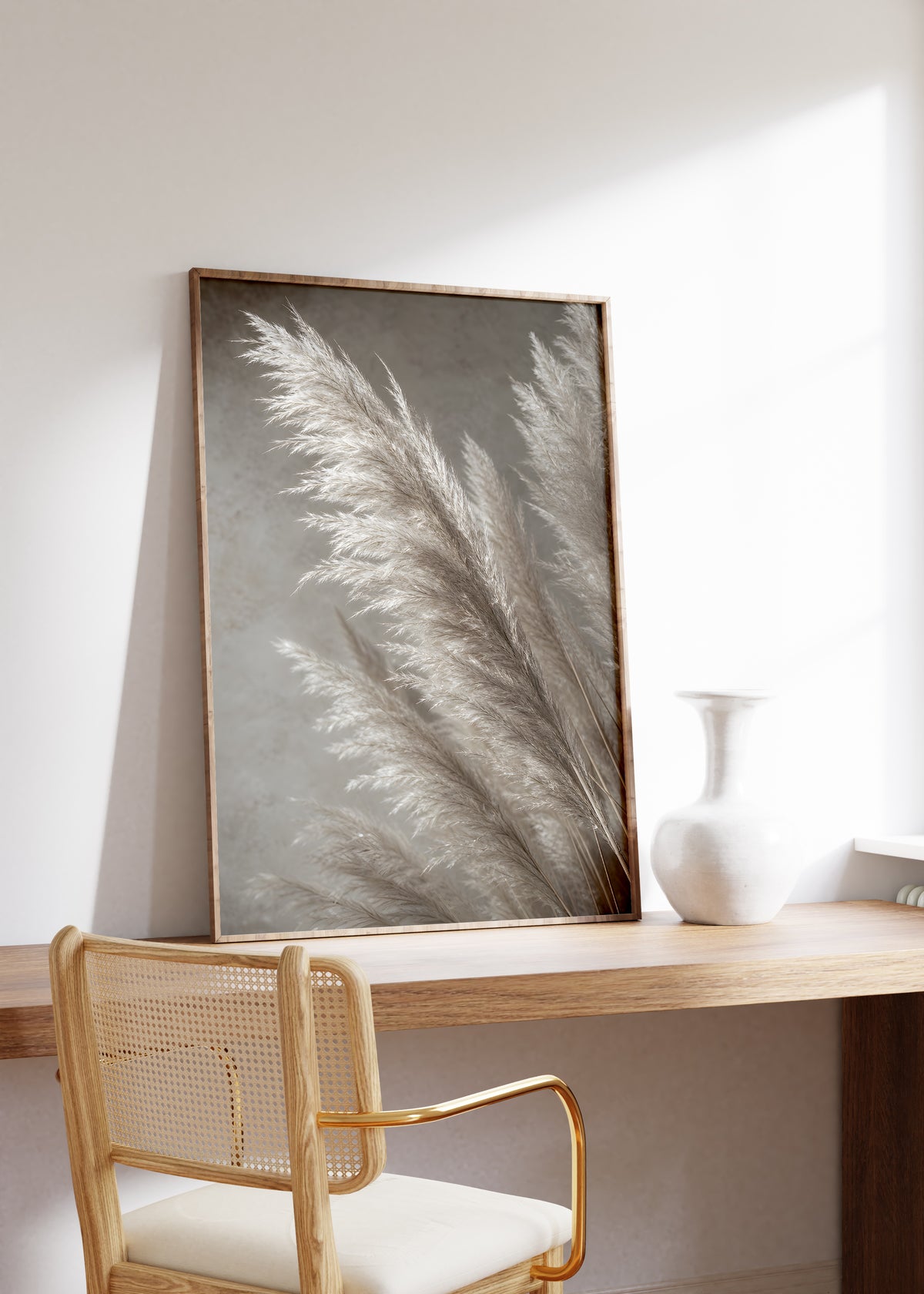 Gerahmtes Poster mit silbrig hellen Pampaswedeln vor grauem Hintergrund, auf einem Holztisch neben einer weißen Vase.