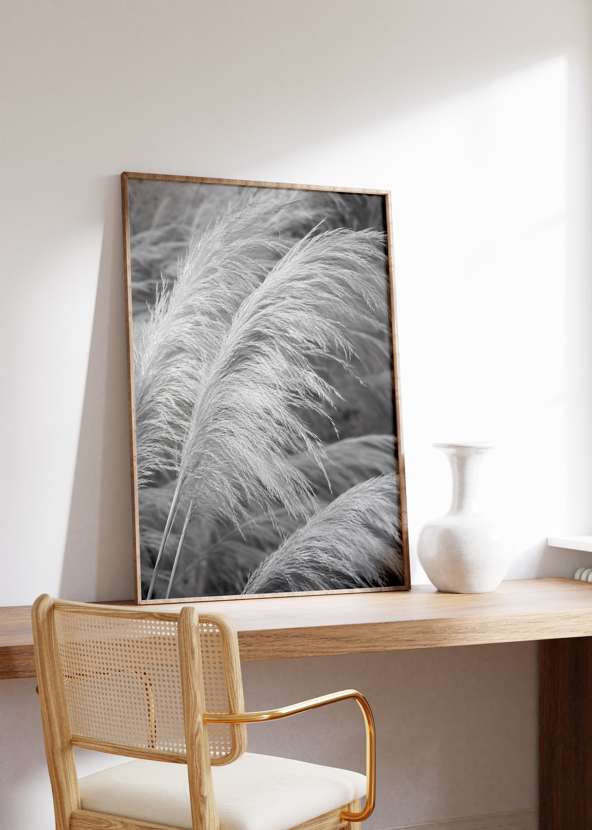 Gerahmtes Poster mit weichen hellen Pampaswedeln in einer Schwarzweiß-Nahaufnahme, auf einem Holztisch neben einer weißen Vase.