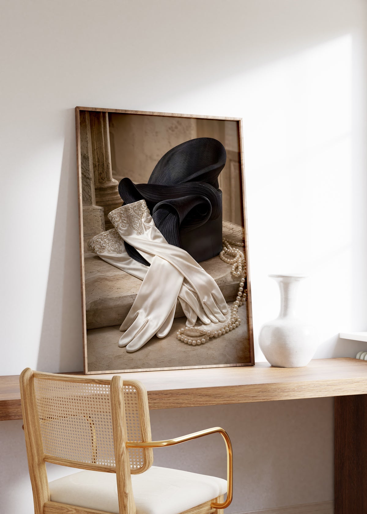 Gerahmtes Poster mit einem Paar weißer Satinhandschuhe neben einem schwarzen Hut und Perlenketten, auf einem Holztisch neben einer weißen Vase.