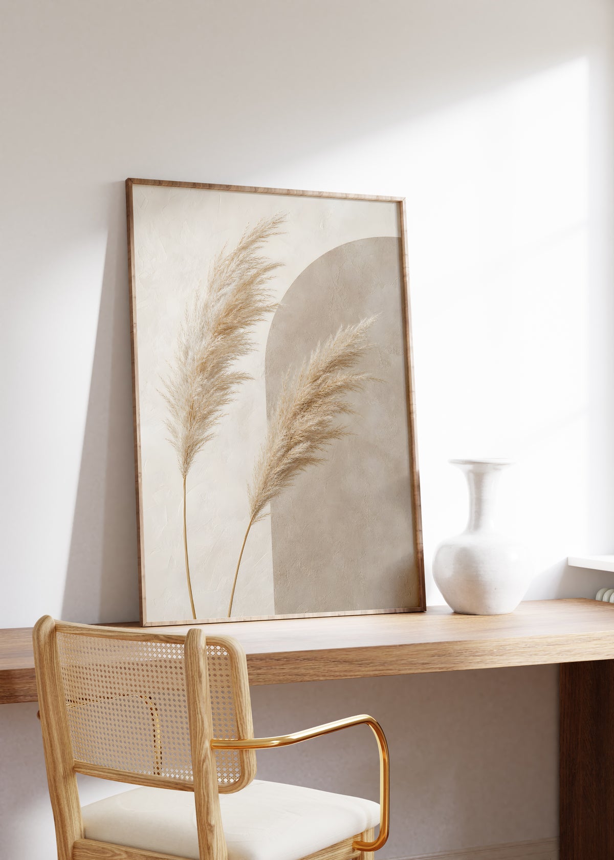 Gerahmtes Poster mit zwei Pampaswedeln vor einer graubeigen Bogenform, auf einem Holztisch neben einer weißen Vase.