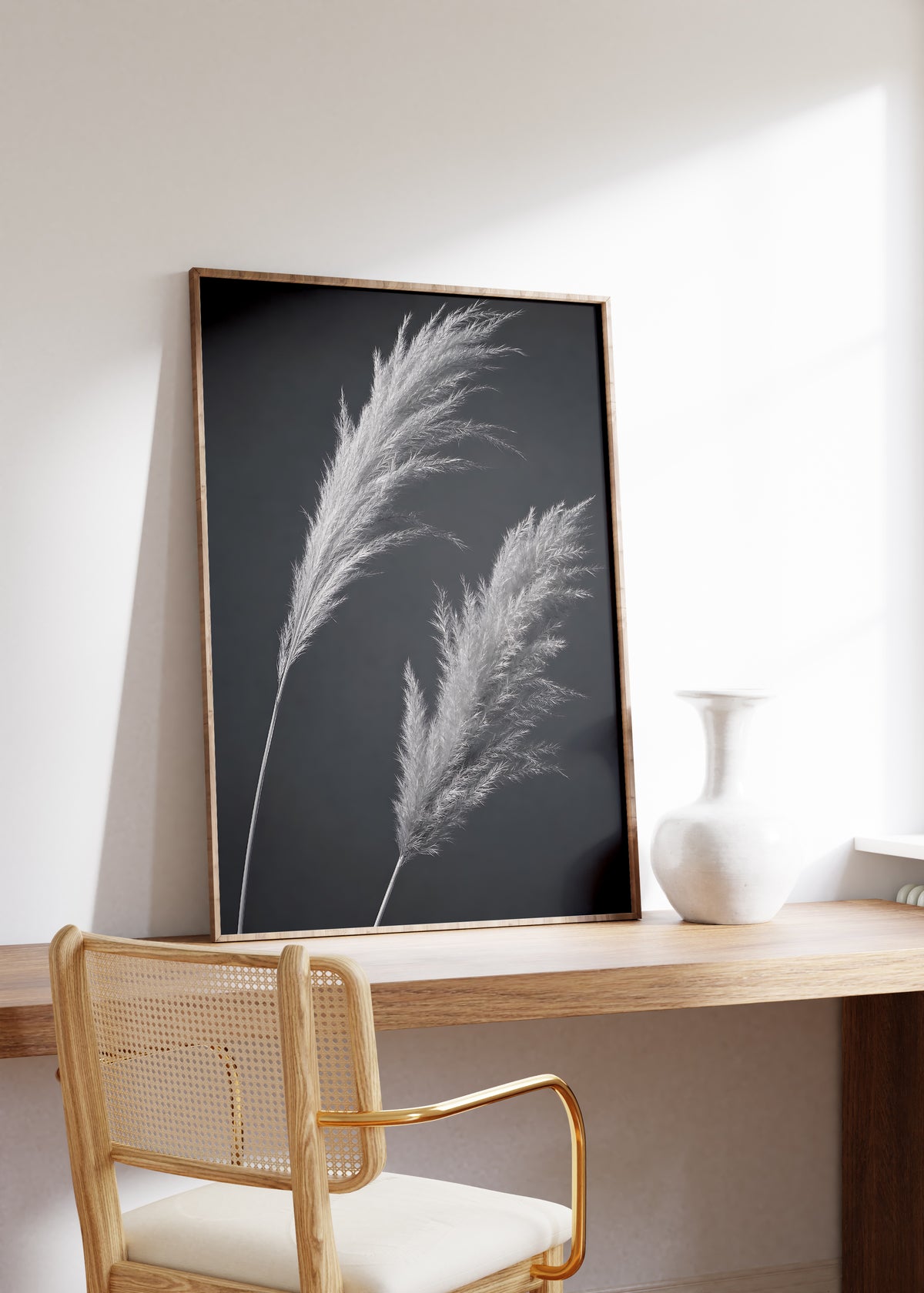 Gerahmtes Poster mit zwei silbrigen Pampaswedeln vor anthrazitfarbenem Hintergrund, auf einem Holztisch neben einer weißen Vase.