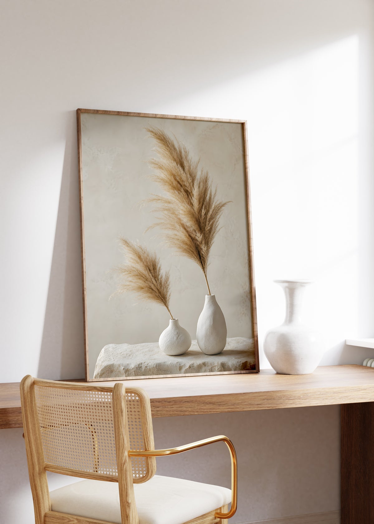 Gerahmtes Poster mit zwei weißen Vasen mit unterschiedlich hohen braunbeigen Pampaswedeln, auf einem Holztisch neben einer weißen Vase.